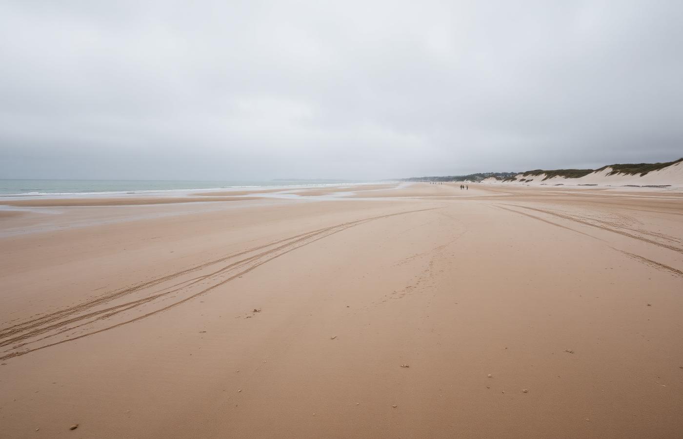 Amplia playa de arena en la costa de Normandía bajo un cielo gris
